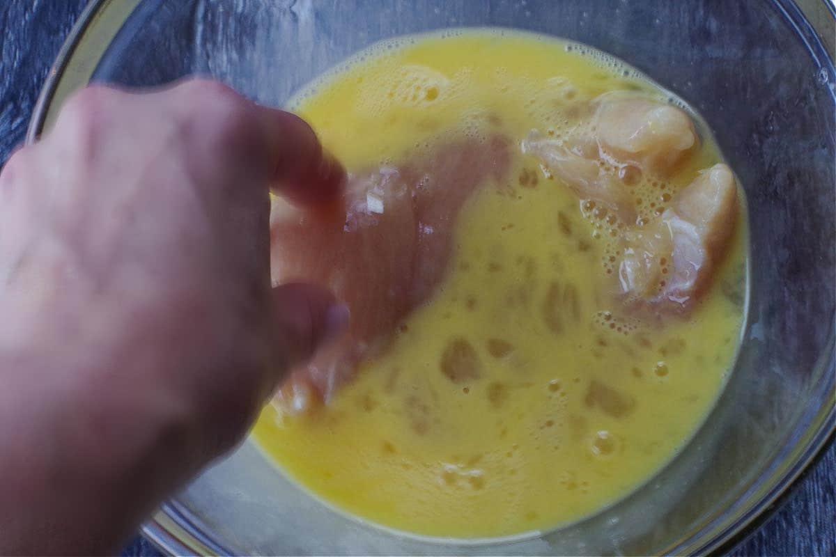 chicken breast being dipped in eggs in glass bowl