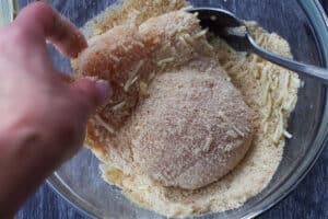 egg coated chicken being dipped in bread crumb mixture