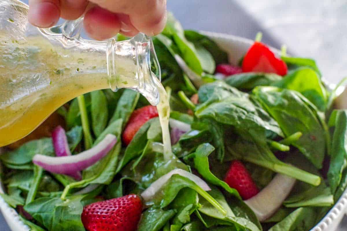 cilantro honey lime dressing being poured onto spinach strawberry pecan salad