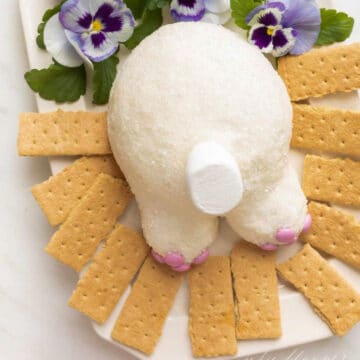 bunny butt cheeseball on a white platter with graham crackers and pansy flowers in the background