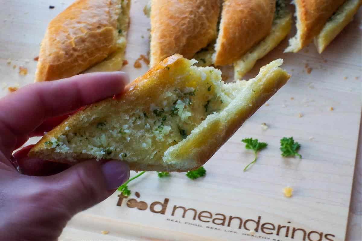 a slice of baguette garlic bread being held up over a customized cutting board