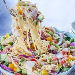 chicken bacon ranch pasta salad being lifted out of a flowered bowl with salad utensils