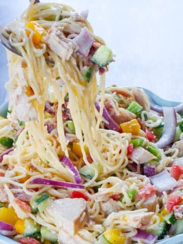 chicken bacon ranch pasta salad being lifted out of a flowered bowl with salad utensils