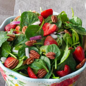 strawberry spinach pecan salad in a large bowl with flower print and wooden utensils
