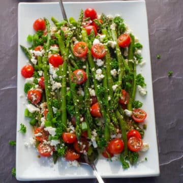 asparagus and tomato salad on a white salad with dressing in the background