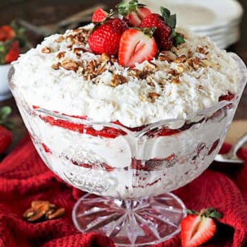 strawberry coconut punch bowl cake on a red material background with strawberries around it