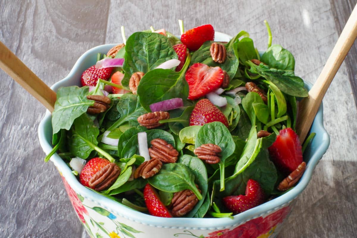 strawberry spinach pecan salad in a large bowl with flower print and wooden utensils