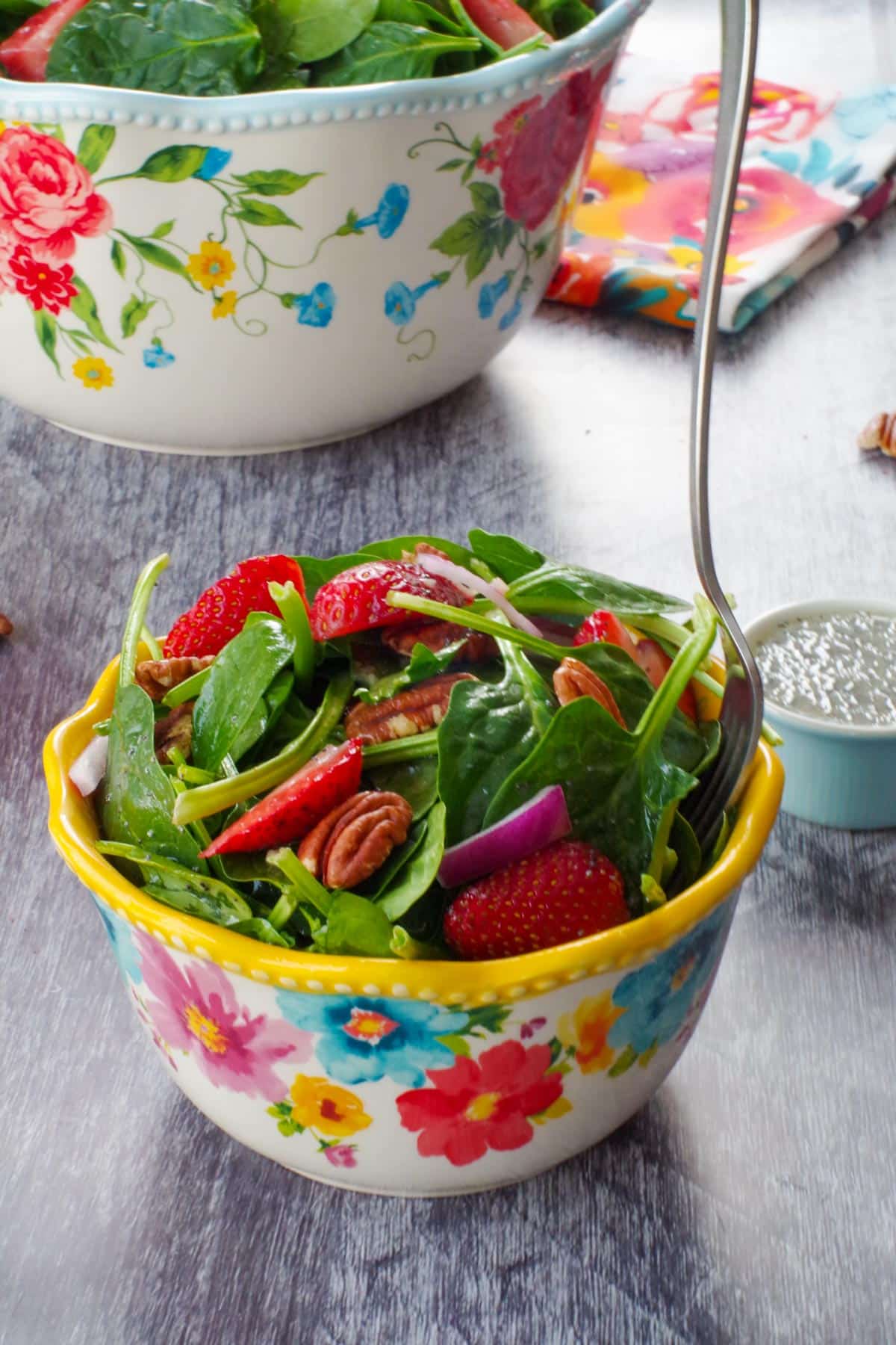 strawberry spinach pecan salad in a small yellow-rimmed flowered bowl with a fork and a large bowl of salad in the background