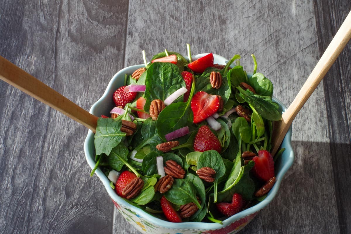 strawberries, spinach, red onion and toasted pecans in a large flowered salad bowl with wooden utentils