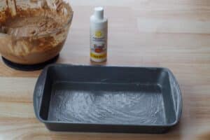 greased cake pan with a bottle of cake release and a bowl of batter in the backgroun