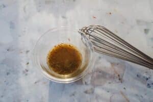 dressing ingredients whisked together in a glass bowl with whisk on the side