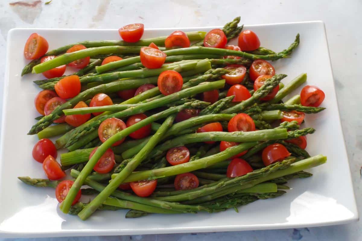 asparagus with grape tomatoes on a white platter