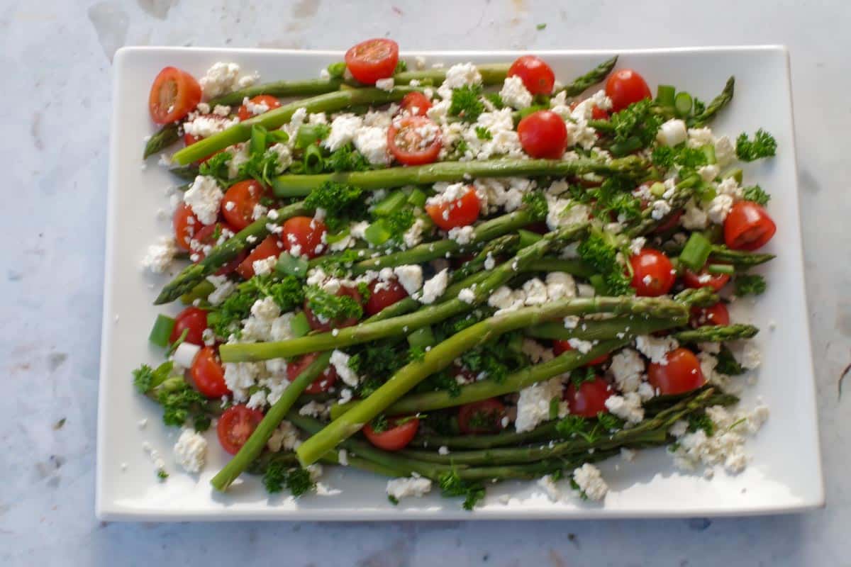 feta cheese and parsley sprinkled on asparagus and tomatoes on white platter