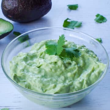 avocado cream sauce in a glass bowl with an avocado in the background