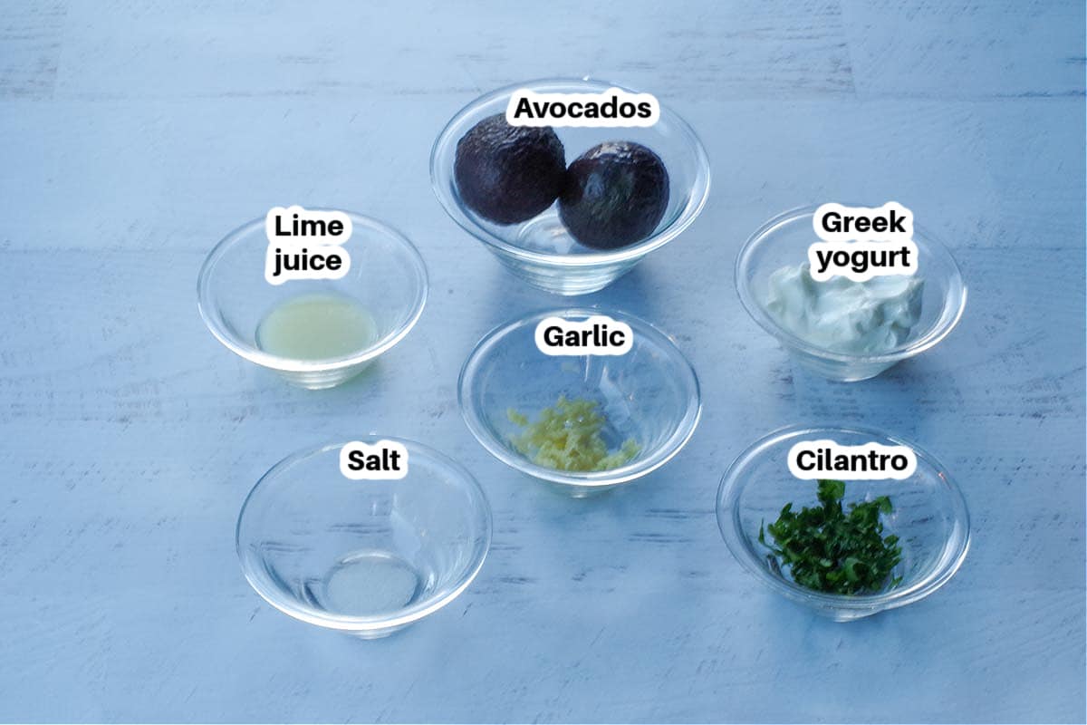 ingredients in avocado cream sauce in glass bowls, labelled, on a faux white wood surface
