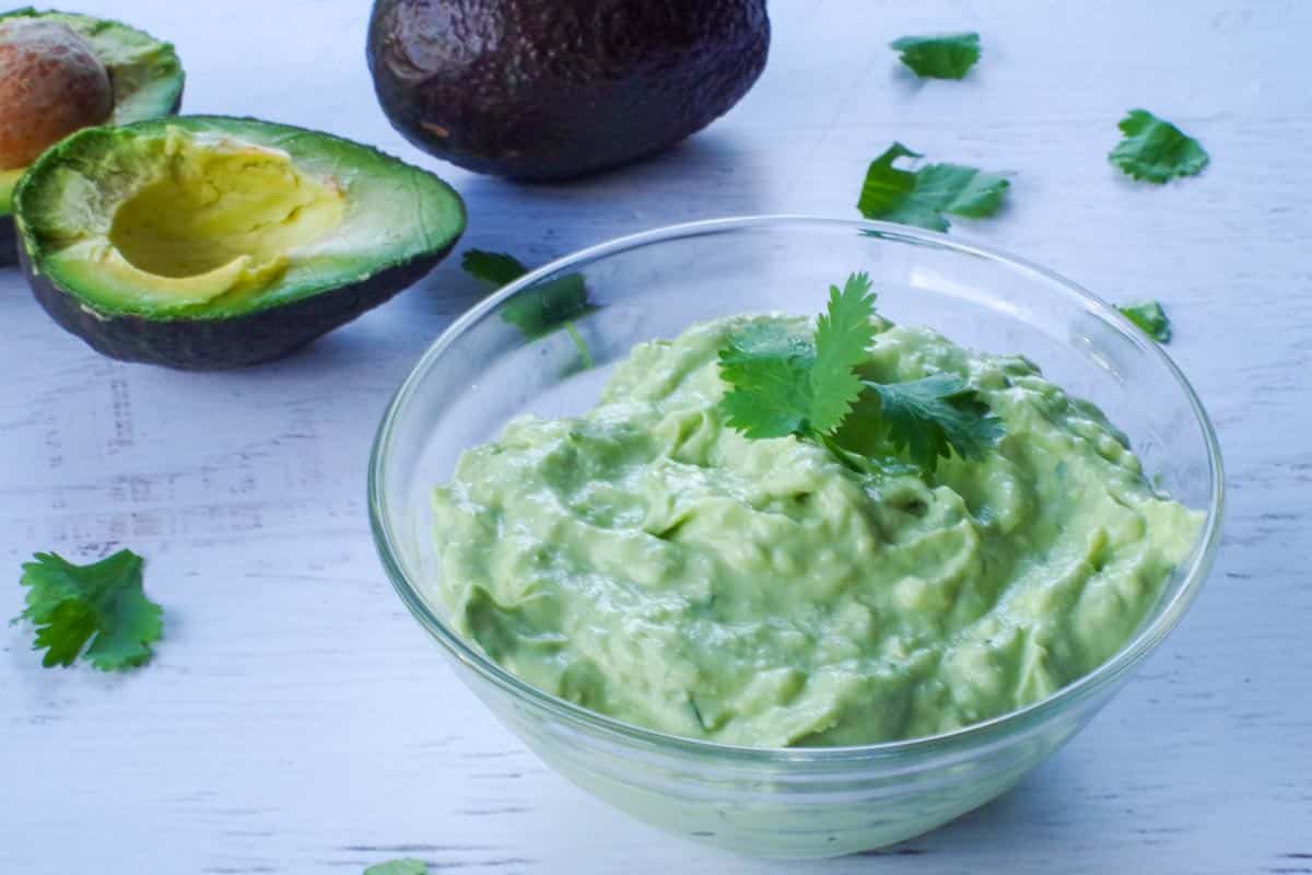 avocado cream sauce in a glass bowl with an avocado in the background