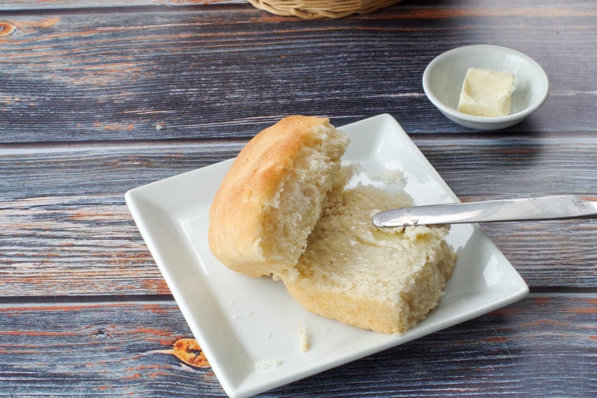 granny bun, split in half, with butter on one half, on a square white plate, with a dish a butter in the background