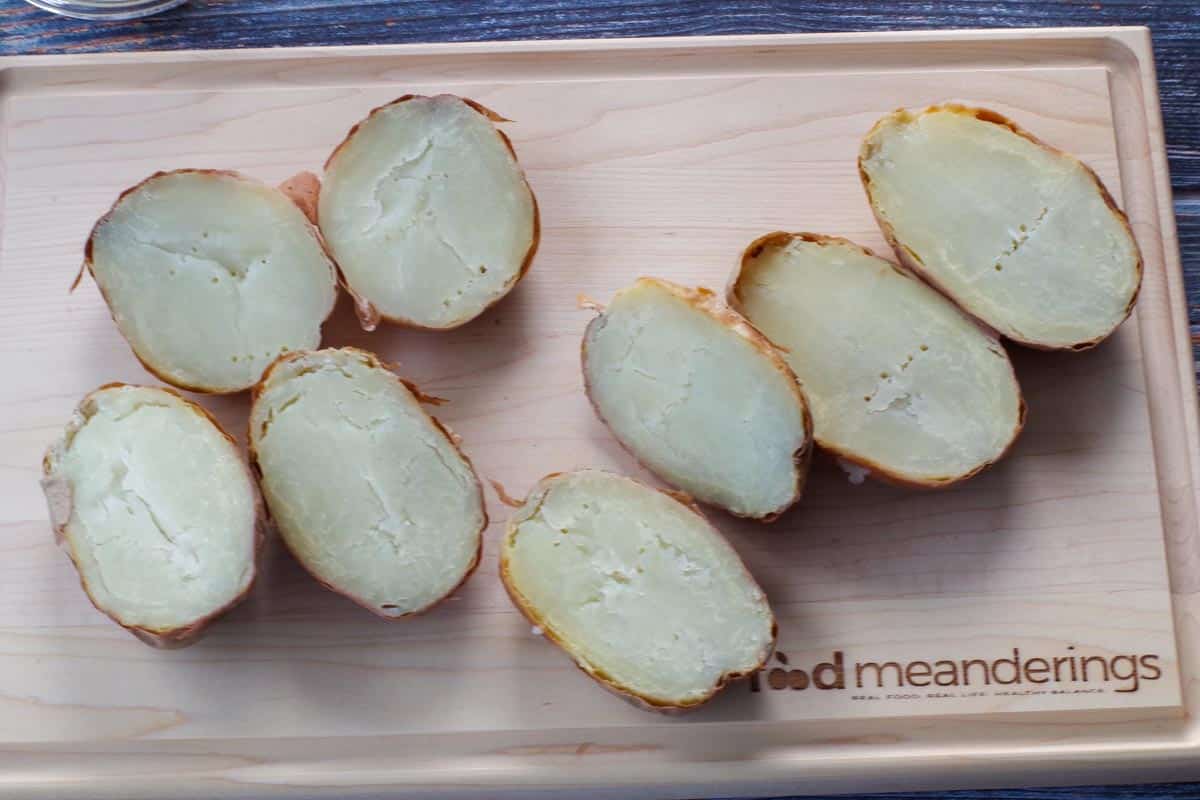 potatoes cut in half, lengthwise, on a wooden cutting board
