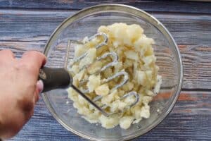 Potato flesh being mashed with potato masher in glass bowl