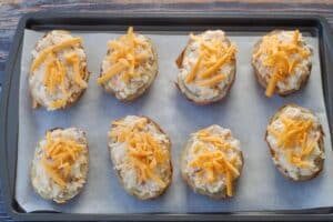 Twice baked caesar potatoes in a parchment lined baking sheet with reserved cheese sprinkled on