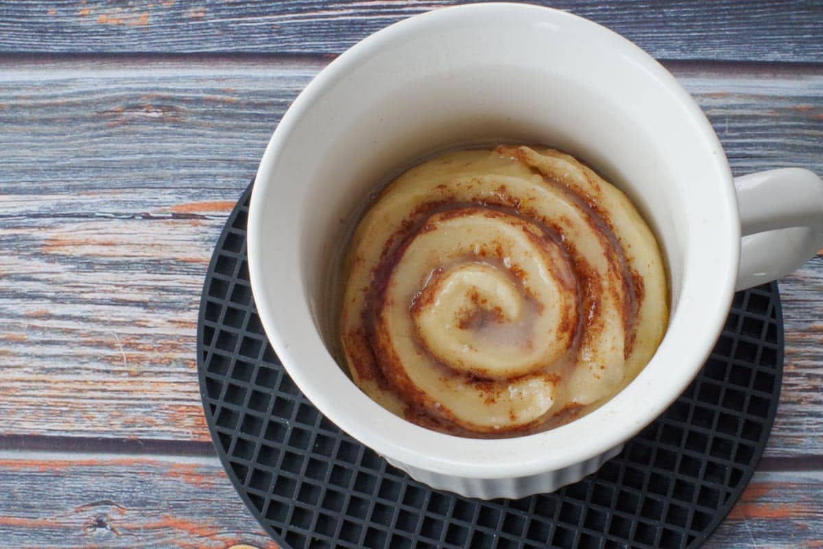 cinnamon roll in a white meal mug on a black round trivet