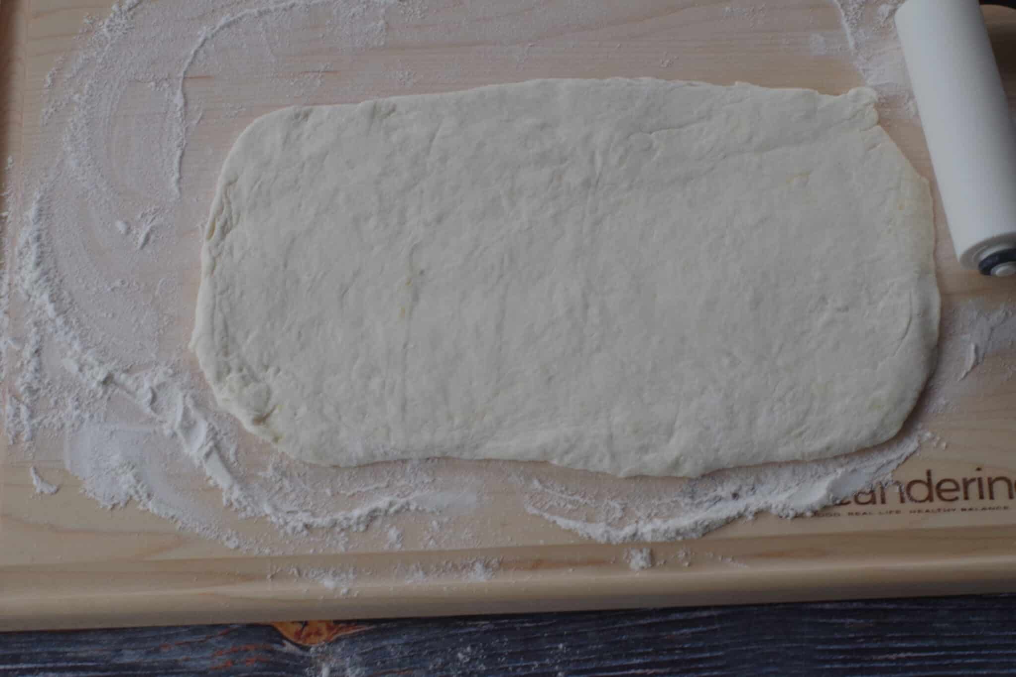 dough rolled out on to a floured wooden cutting board