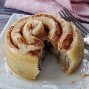 healthy cinnamon roll in a mug cut open on a white plate, with a pink napkin in the background