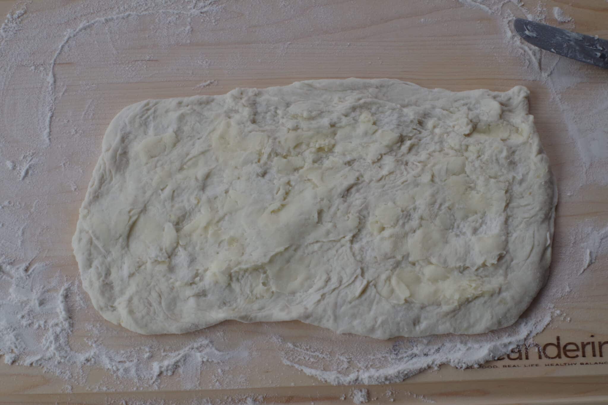 butter spread over the dough rectangle on a wooden cutting board