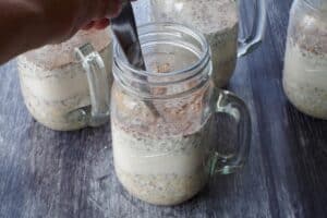 Milk being mixed into oat mixture in glass mason jar mugs