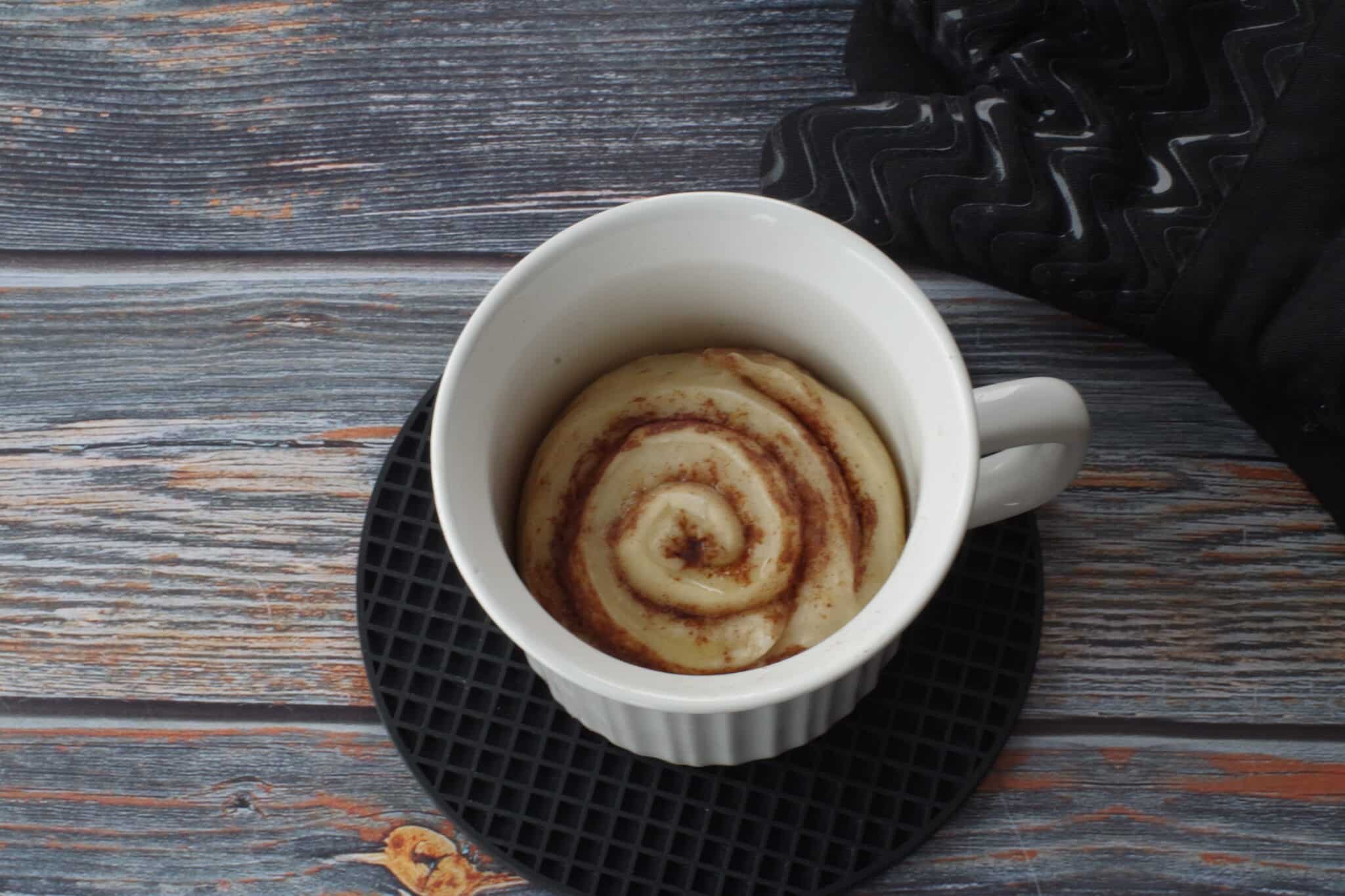 Baked cinnamon roll in meal mug on black round trivet