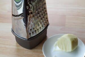 box grater beside ½ a grated potato on a white plate