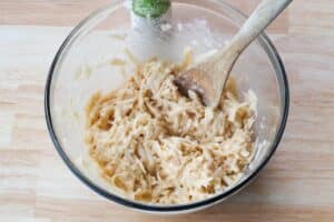shredded potatoes mixed with other ingredients in a large glass bowl with a wooden spoon