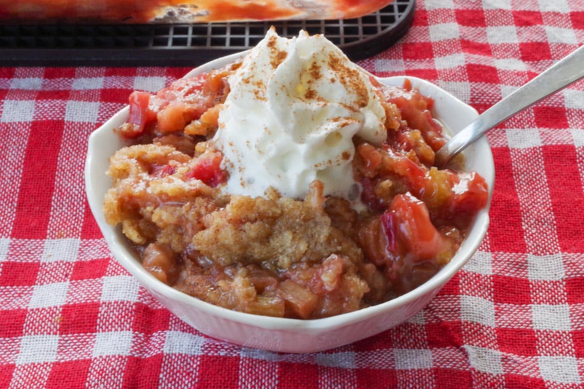 rhubarb crumble topped with whipped cream, in a white petal dish with a spoon 