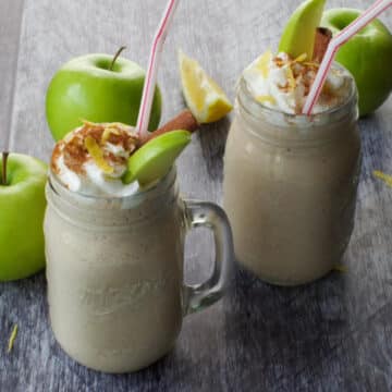 2 apple pie smoothies in mason jar mug with green apples in the background