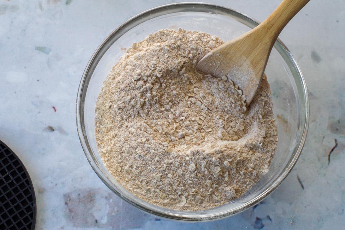 brown sugar, baking soda, oats and flour in a glass bowl with a wooden spoon