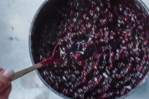 Saskatoon berry square filling being held up on a spoon over a saucepan of berry filling