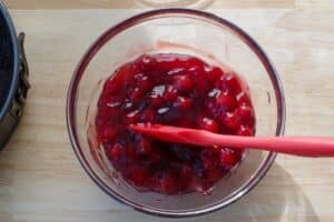 cherry pie filling mixed with gelatin and almond extract in glass bowl, with red spatula
