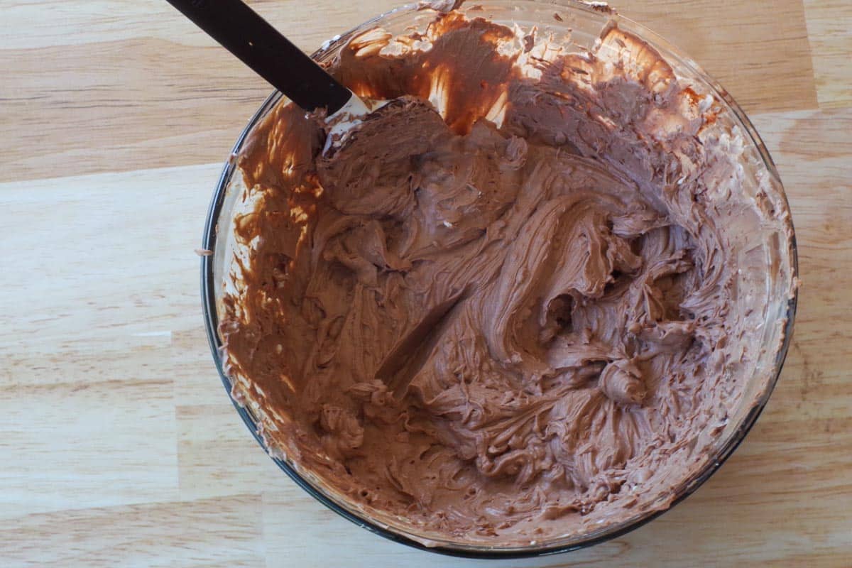 chocolate and gelatin mixed in with cream cheese and sugar in large glass bowl, with black spatula