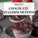 Healthy Chocolate Zucchini Muffins in a muffin tin , with one on top and strawberries and a zucchini in the background