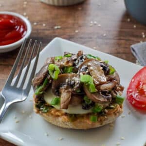 mozza mushroom breakfast sandwich on a white plate with tomato and a dish of ketchup in the background