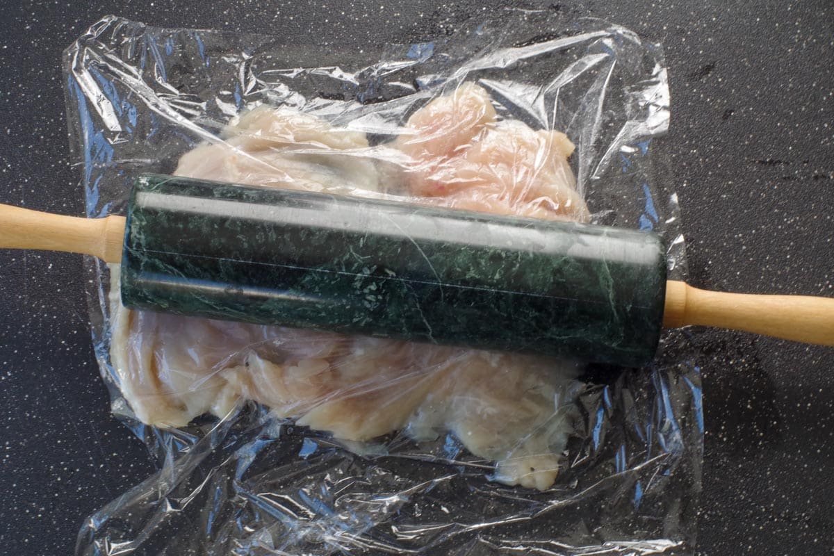 chicken breast being pounded down with rolling pin