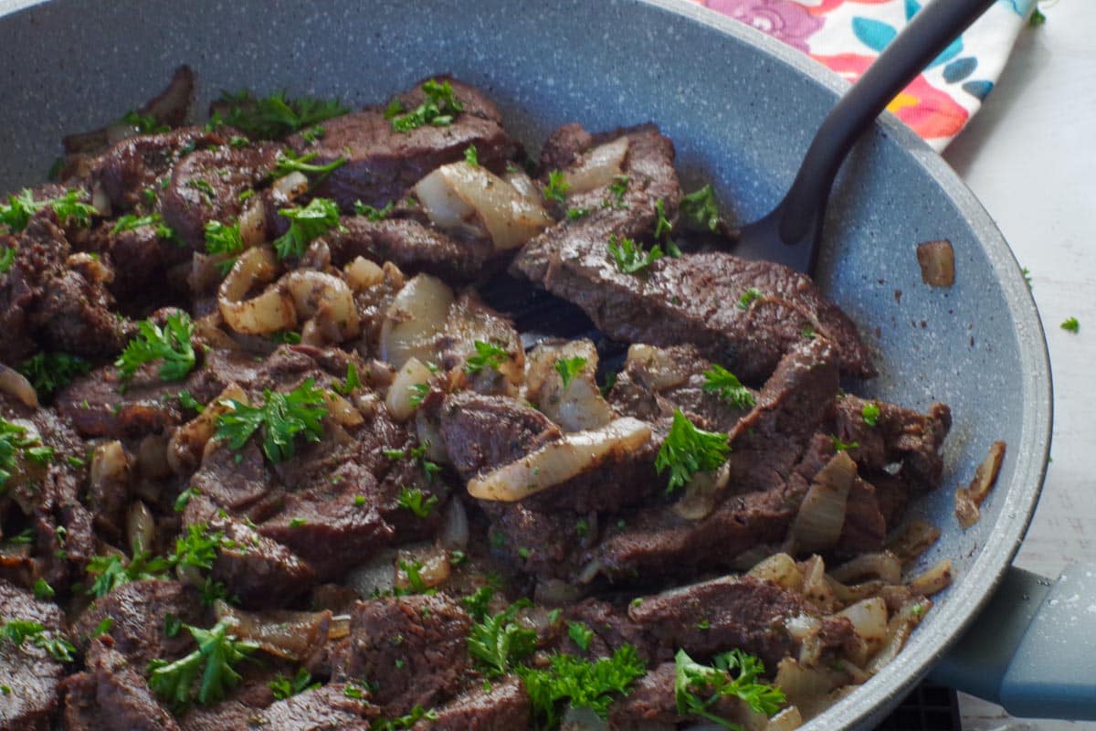 cooked venison steak in a skillet with a spatula turner