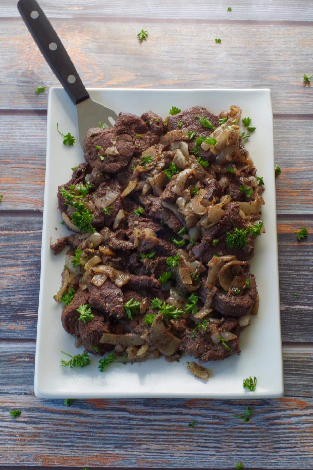 cooked venison steak on a white platter with a turner spatula