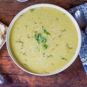 Zucchini Potato soup in a beige bowl with blue paisley napkin and spoon on the side