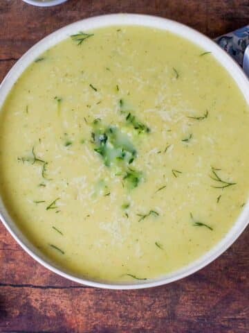 Zucchini Potato soup in a beige bowl with blue paisley napkin and spoon on the side