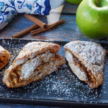 apple cinnamon scones on a black serving platter with a green apple and blue paisley patterned oven mitts in the background