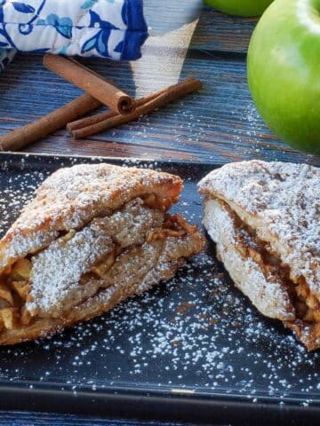 apple cinnamon scones on a black serving platter with a green apple and blue paisley patterned oven mitts in the background