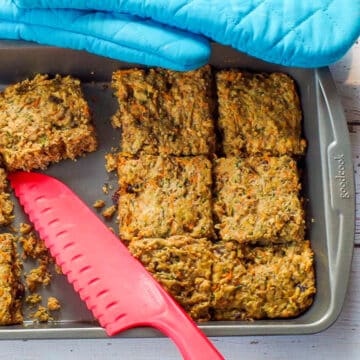 Zucchini bars cut in a pan, with some missing and a red silicone knife