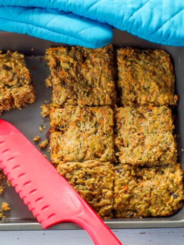 Zucchini bars cut in a pan, with some missing and a red silicone knife