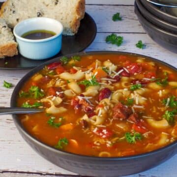 leftover ham macaroni soup in a black bowl, with more black bowls in the background and onion and olive bread with bread and oil